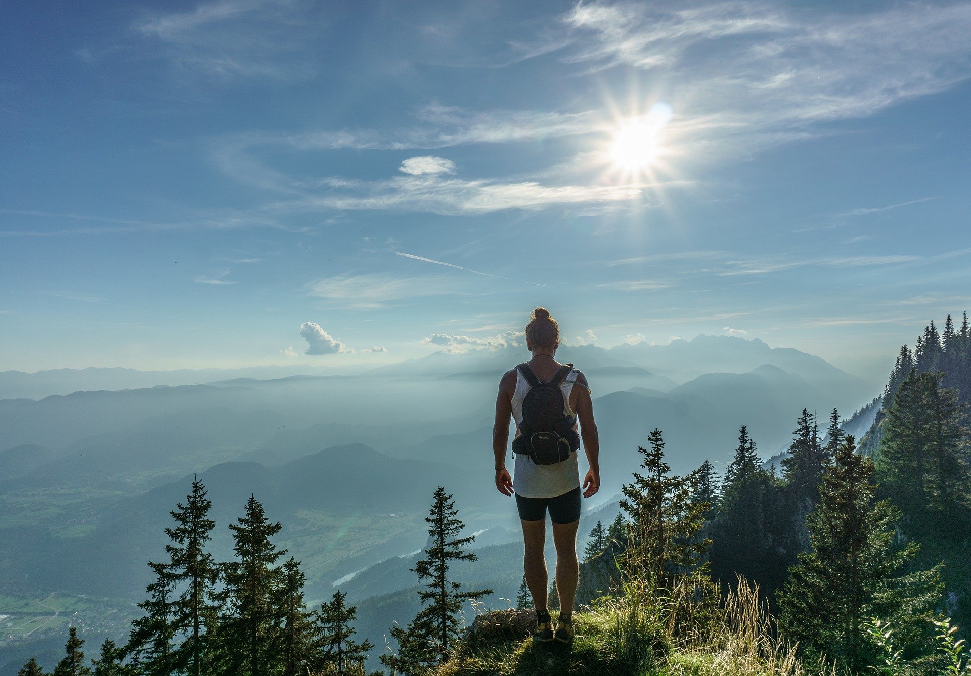 Foto de uma mulher no alto de uma montanha observando o céu e outras montanhas