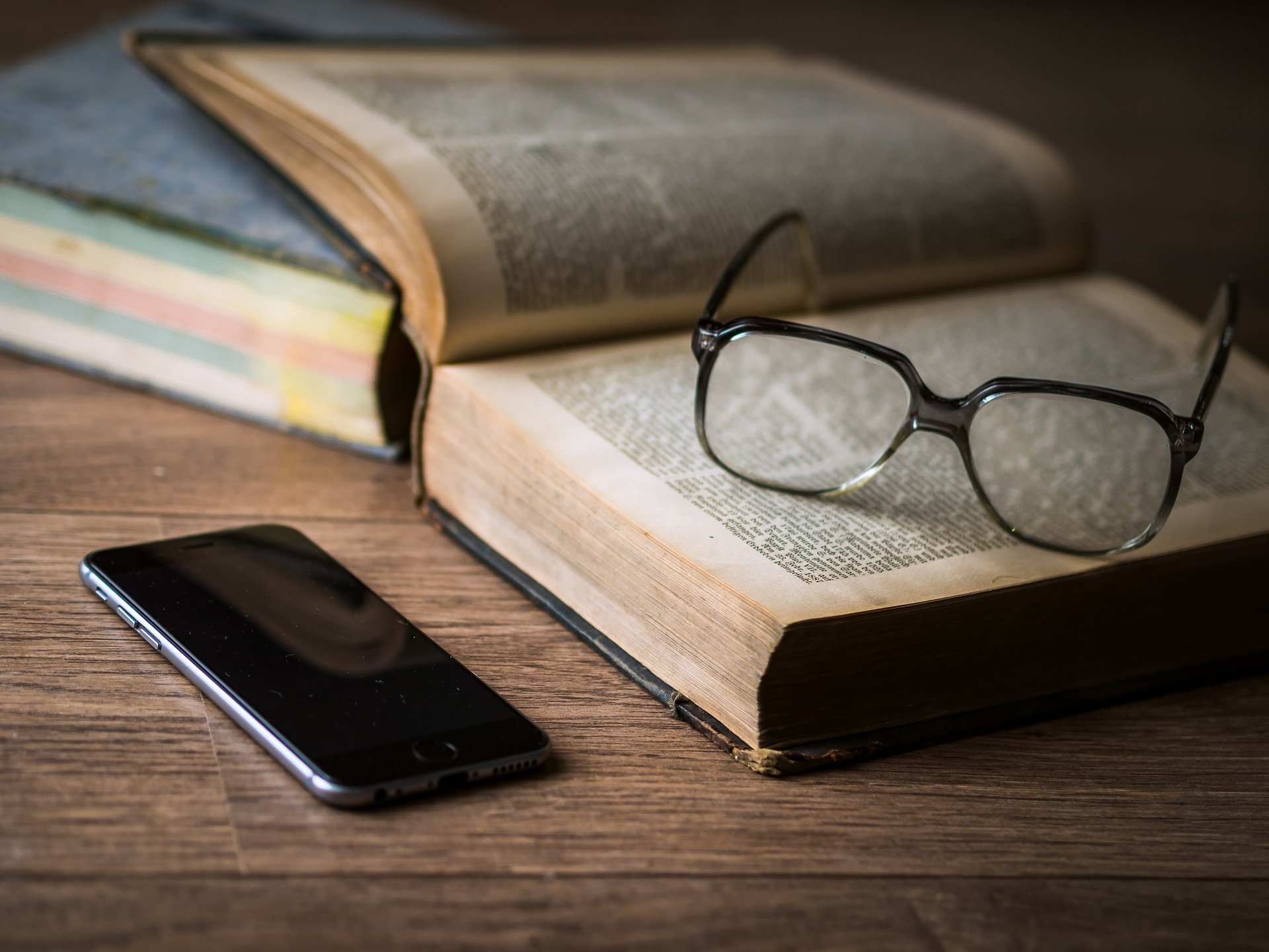 Um óculos em cima de um livro, e um celular ao lado.