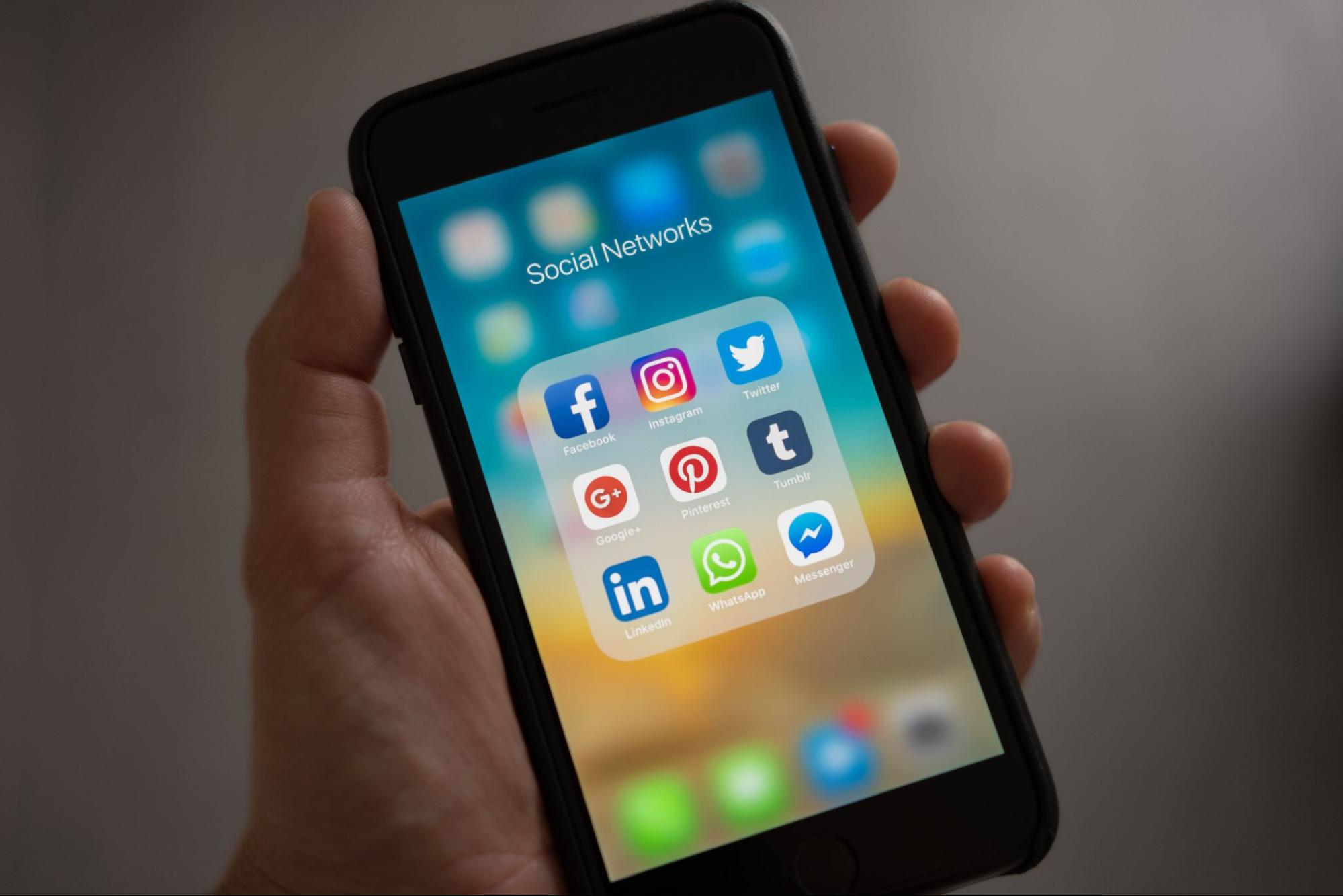 Mão segurando iphone mostrando uma pasta com redes sociais.