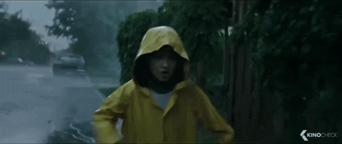 Gif de um garoto na chuva, vestindo uma capa de chuva amarela, correndo atrás do seu barquinho de papel que é levado pela correnteza e cai em um bueiro.