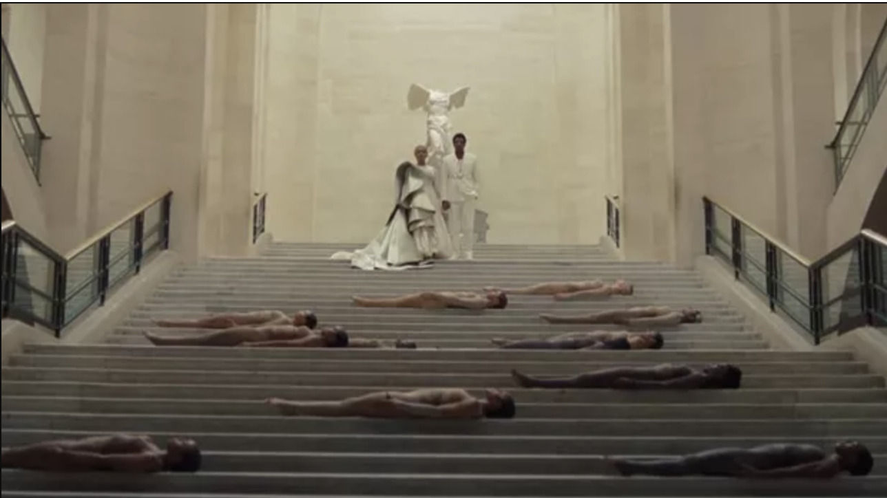 Escadaria do museu do Louvre onde Beyoncé e Jay Z se encontram ao centro e em cima da escada e bailarinos estão deitados espalhados ao longo da escada.