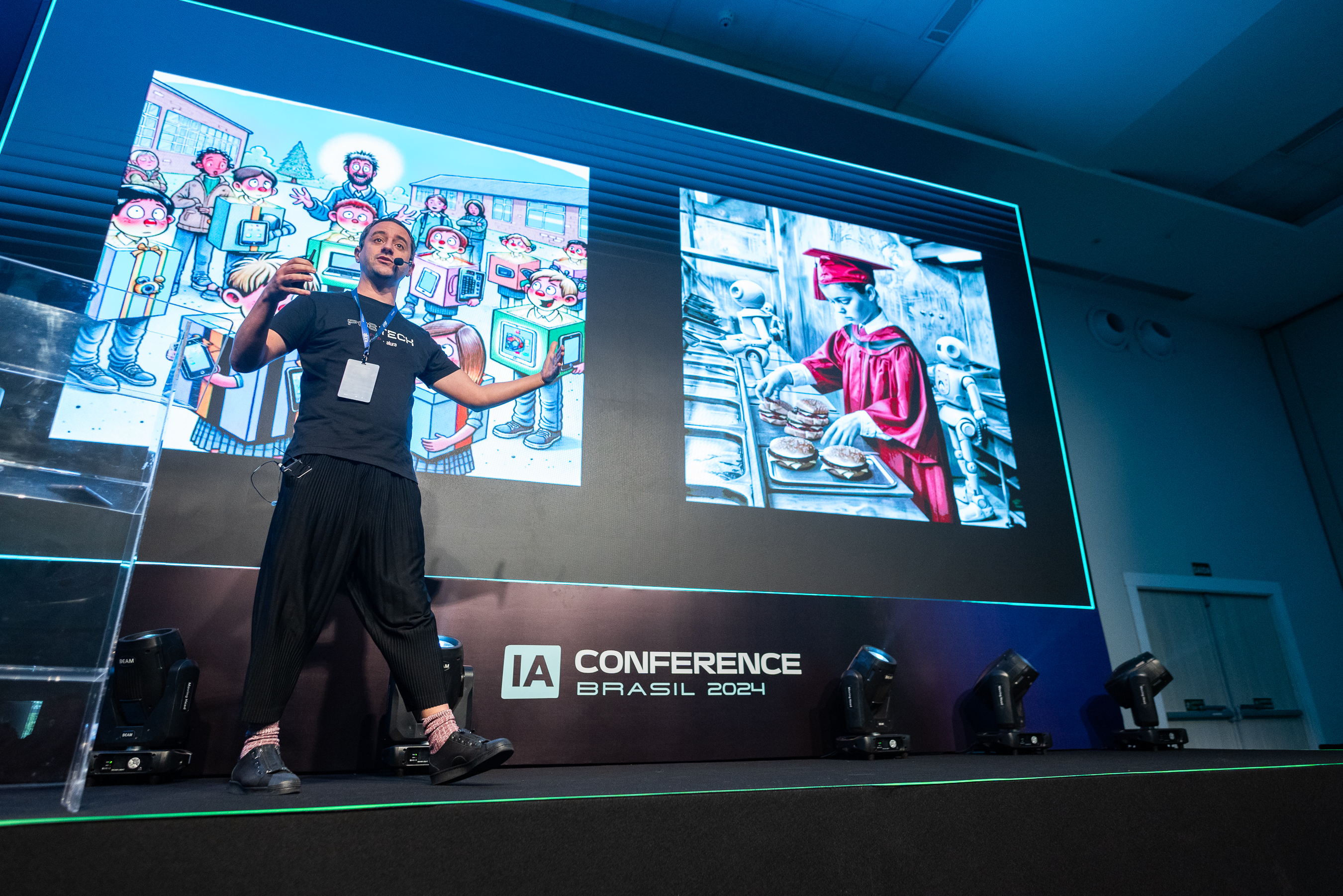 A imagem é uma fotografia de Guilherme Silveira no palco do evento: um homem branco, de cabelo curto e escuro, de camiseta, calça e sapatos pretos e meia vermelha