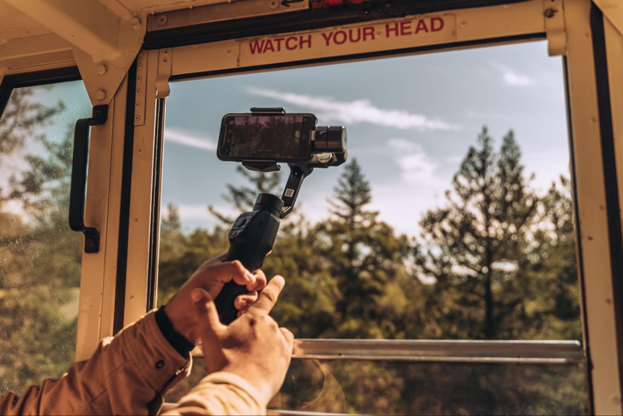 Imagem de uma pessoa segurando um gimbal com um celular e apontando para uma paisagem.
