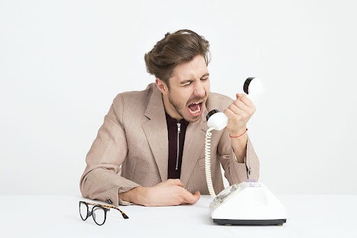 Homem vestindo uma jaqueta de terno marrom gritando em um telefone branco.