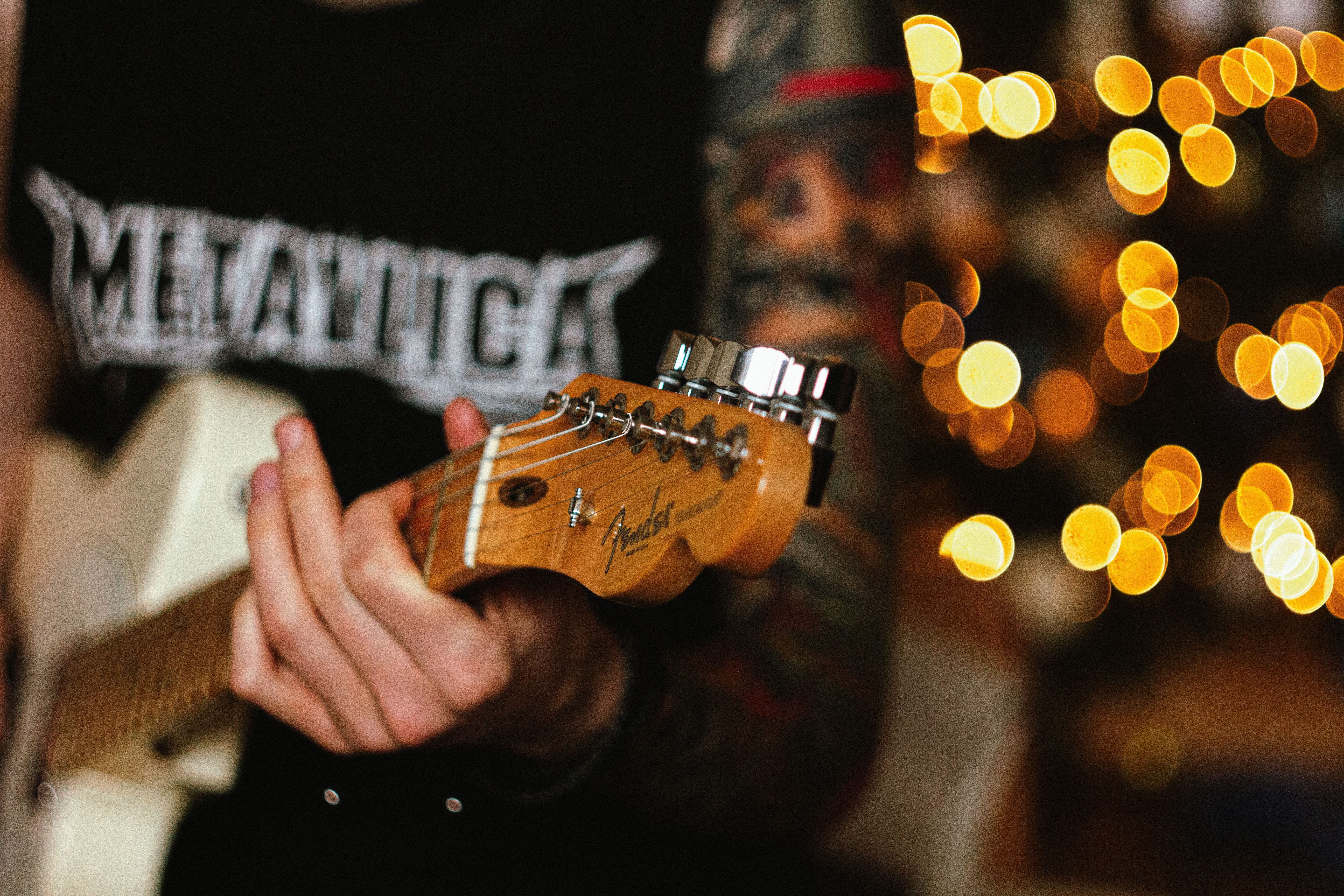 Imagem de um homem tocando sua guitarra e vestido com uma blusa com o nome “Metallica” impresso na frente.