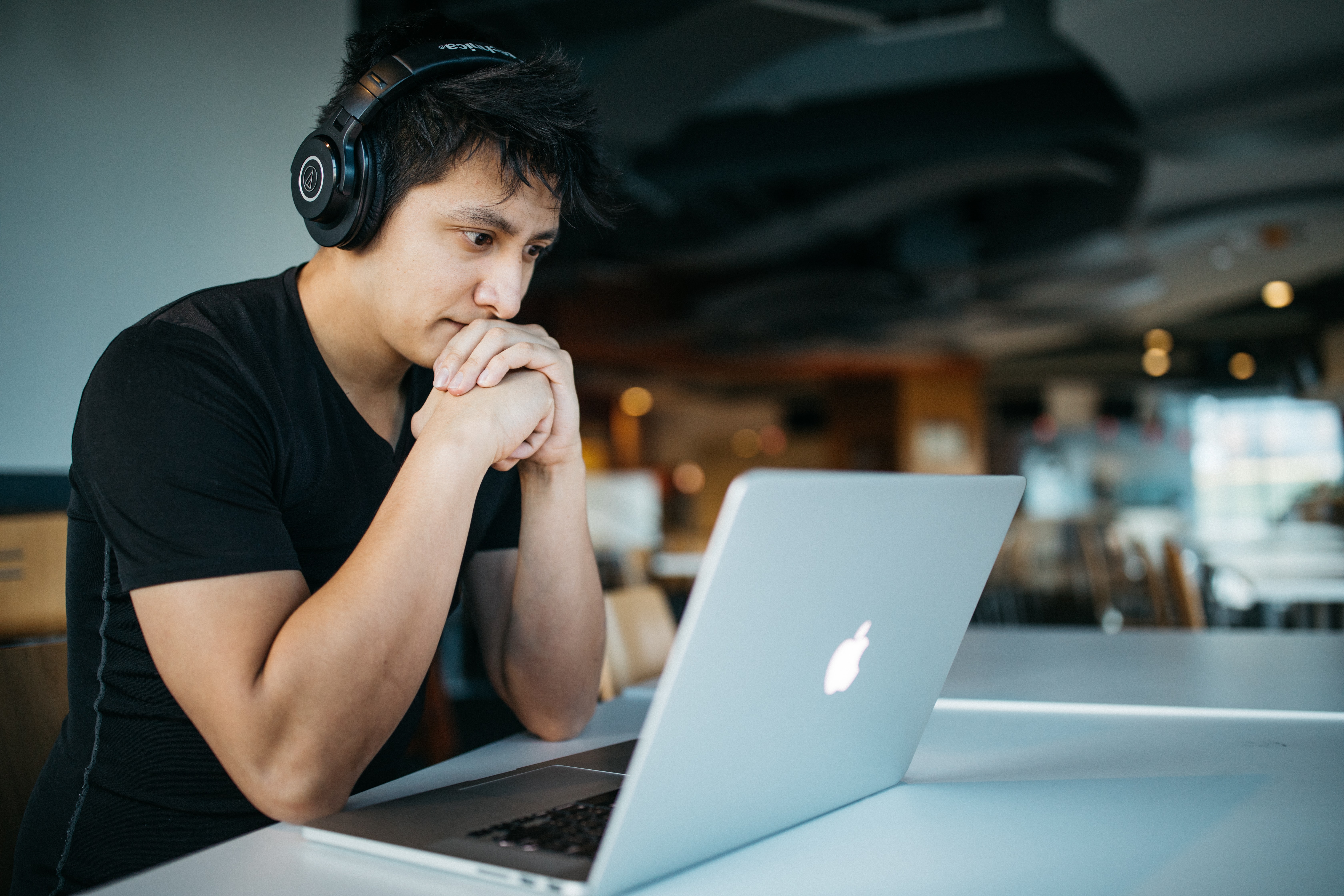 Imagem de um homem sentado de frente para uma mesa utilizando headphones e um notebook