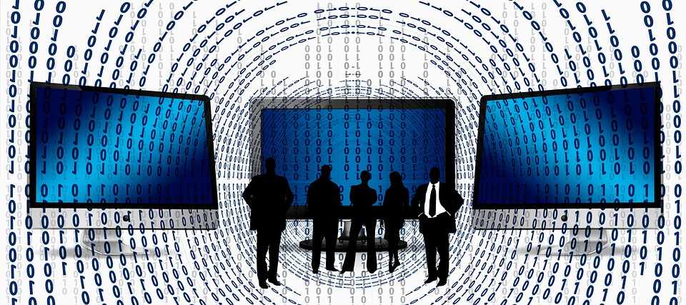 Três pessoas a frente de três monitores, com código binário ao redor deles em formato circular.