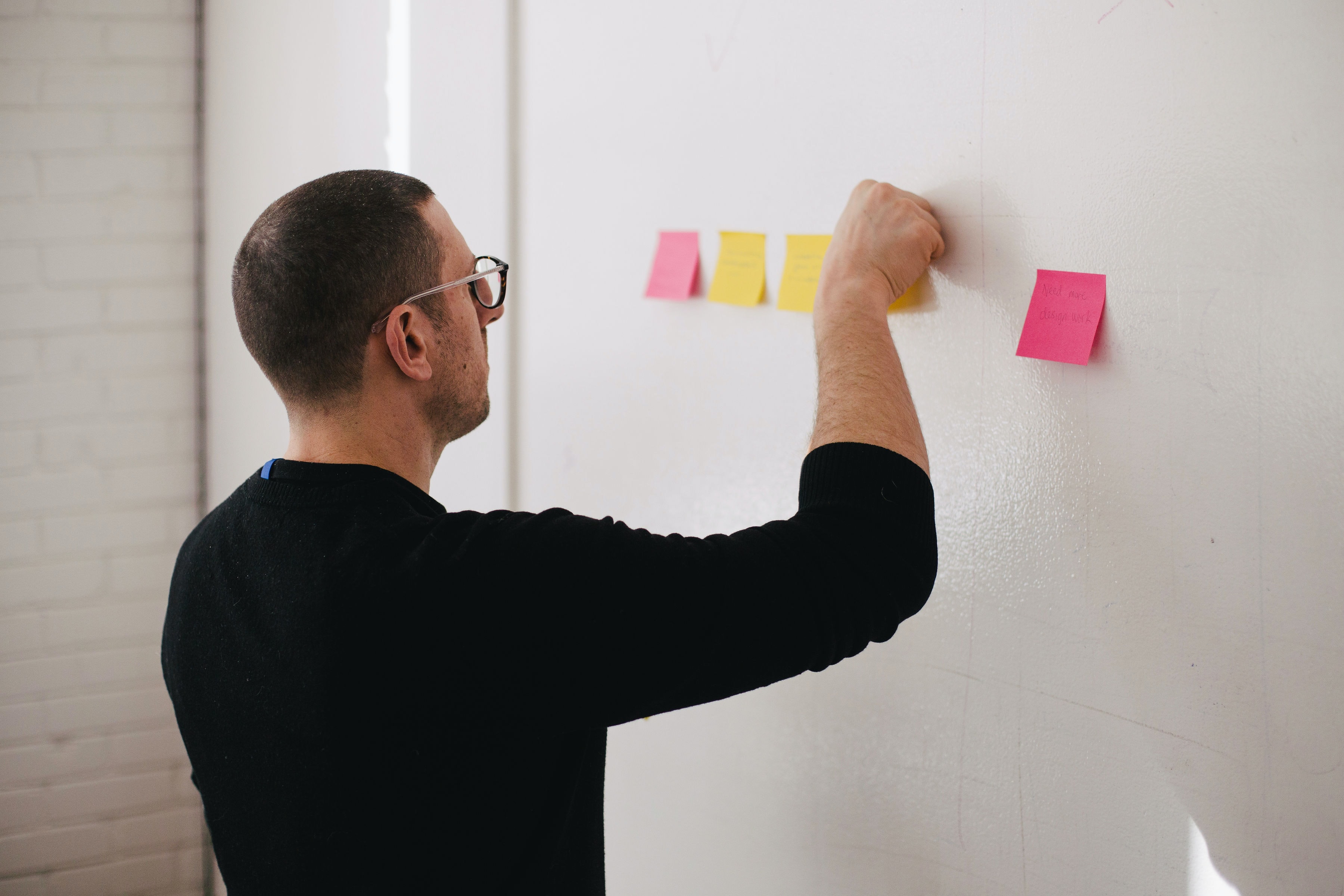 Imagem de uma pessoa de frente para um quadro branco pendurando alguns post-its com anotações.