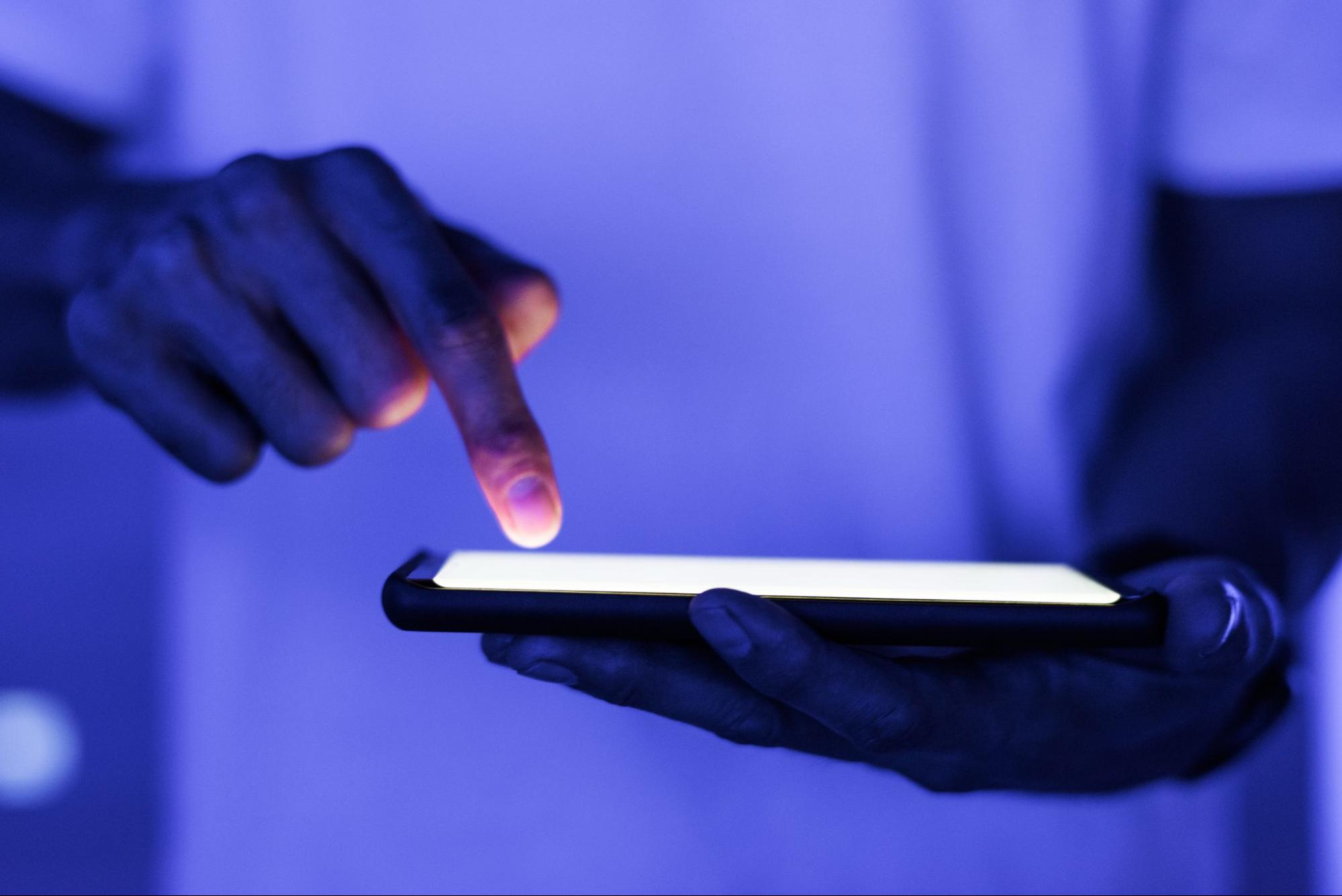 Imagem de uma pessoa mexendo em um smartphone. Destaque para o smartphone e para o dedo indicador da pessoa.
