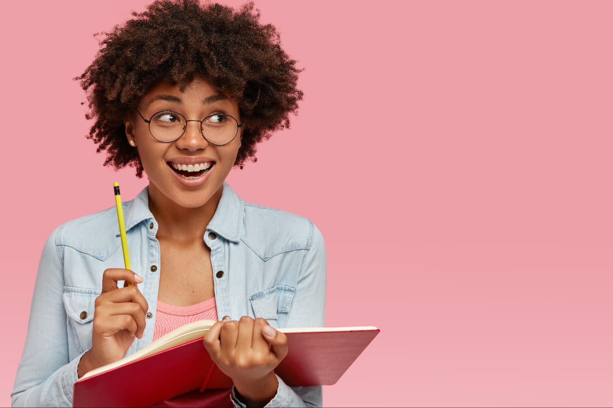 Imagem - Mulher segurando caderno e lápis com olhar de quem teve uma ideia.