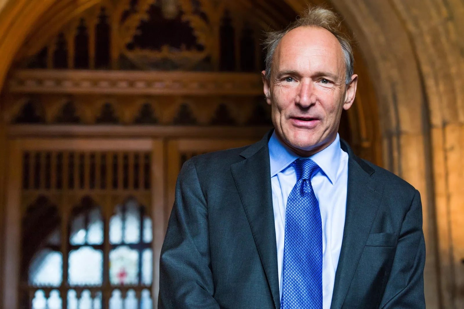 a imagem é uma foto de Tim Berners-Lee, um homem branco de cabelos brancos, olhos claros, vestido com um terno azul marinho, camisa social clara e gravata na cor azul. Fonte: Wikimedia Commons