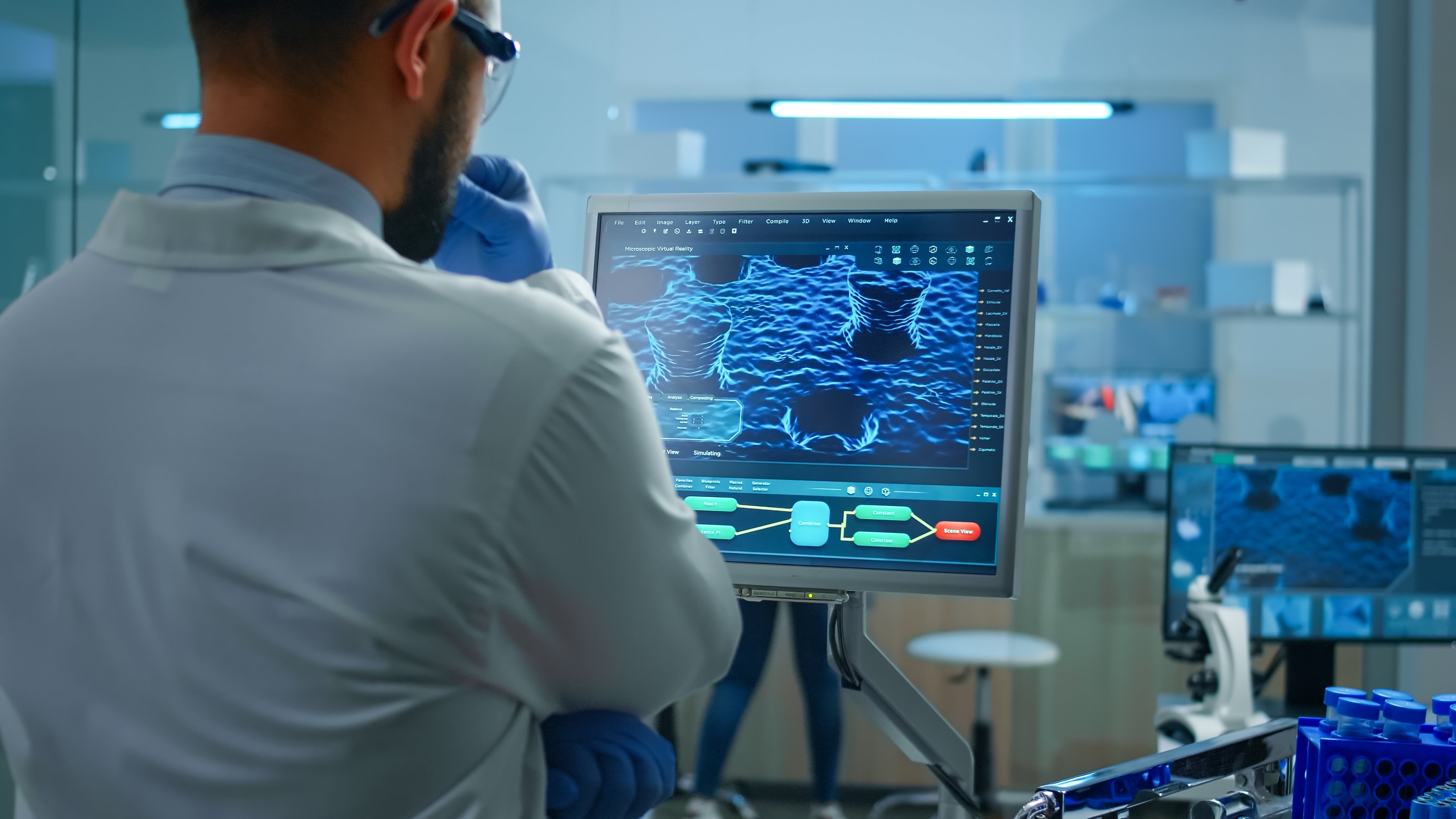 Imagem contendo um médico analisando as imagens em 3D que aparecem em uma tela. No fundo é possível notar que a imagem é ambienta em um laboratório médico.