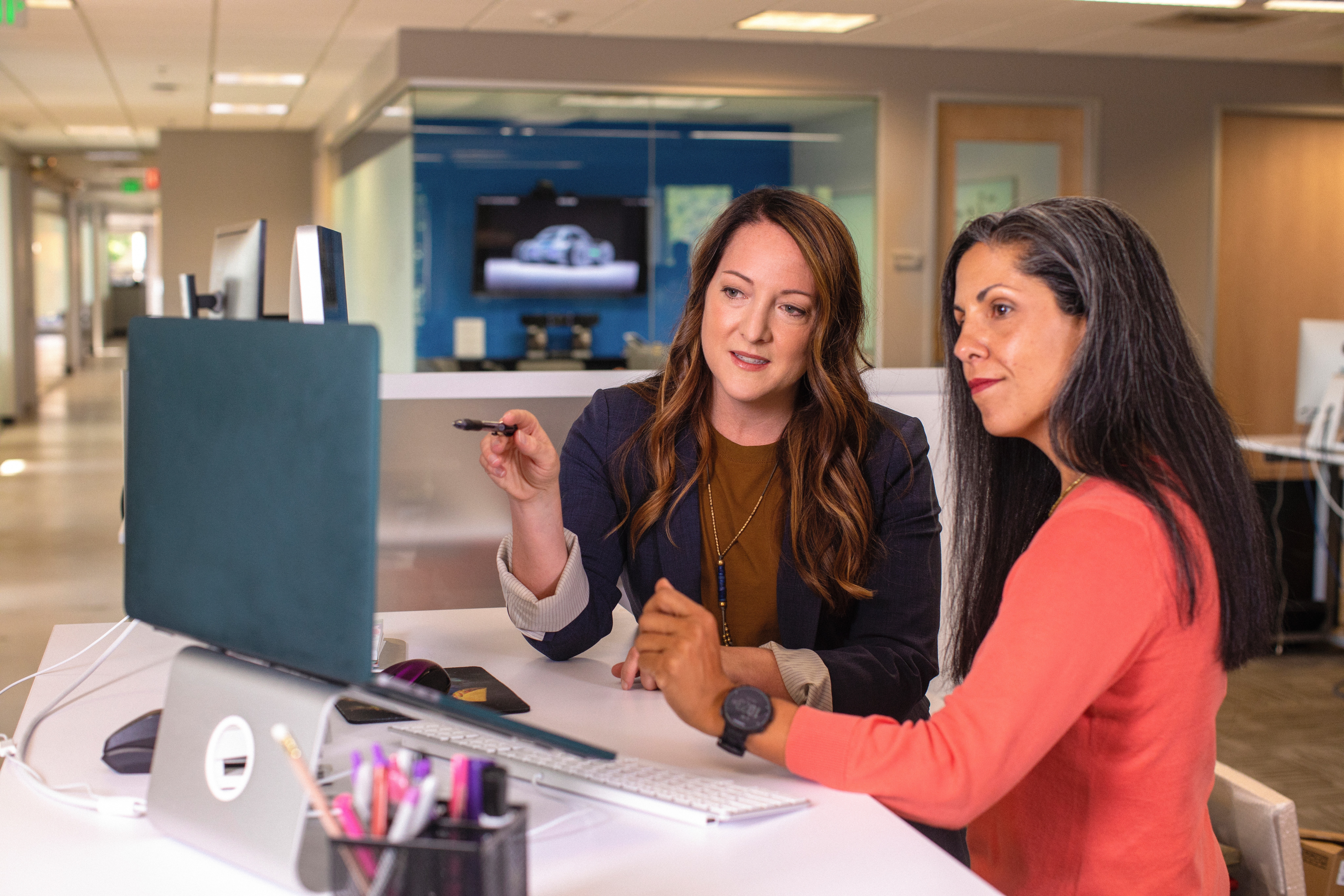 Imagem de duas mulheres em um escritório, na qual uma aponta para a tela de um laptop enquanto a outra observa o que está sendo exibido na tela.