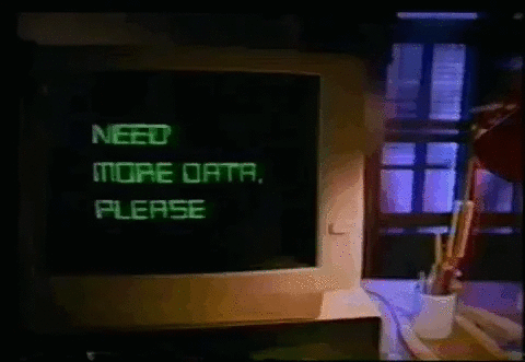 Gif de uma sala com pouca luminosidade mostrando um computador antigo de tubo se movendo sozinho da direita para a esquerda sobre uma mesa, Na tela do computador aparece a frase "Need more data please", ou “Preciso de mais dados, por favor”, em português. Sobre a mesa, no lado direito da imagem, temos uma luminária e um porta-lápis com alguns lápis e canetas dentro dele.