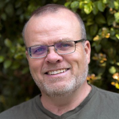 Foto do Rasmus Lerdorf, criador do PHP. Homem de meia idade, caucasiano, de olhos claros e usando óculos de grau, sorrindo, com barba e cabelos curtos grisalho