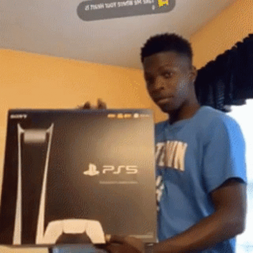 Gif animado que ilustra um homem negro, jovem, que segura uma caixa de Playstation. Ele demonstra estar feliz e veste uma camisa da cor azul, e a caixa do Playstation 5 é da cor preta.