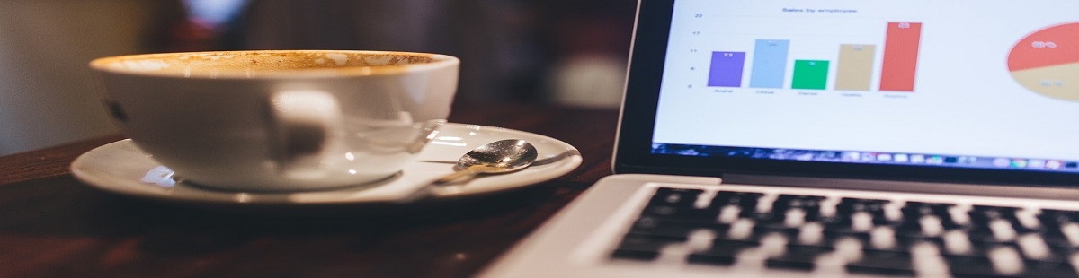 Mesa de trabalho com um notbook transmitindo gráficos, e do lado, uma xícara de café.