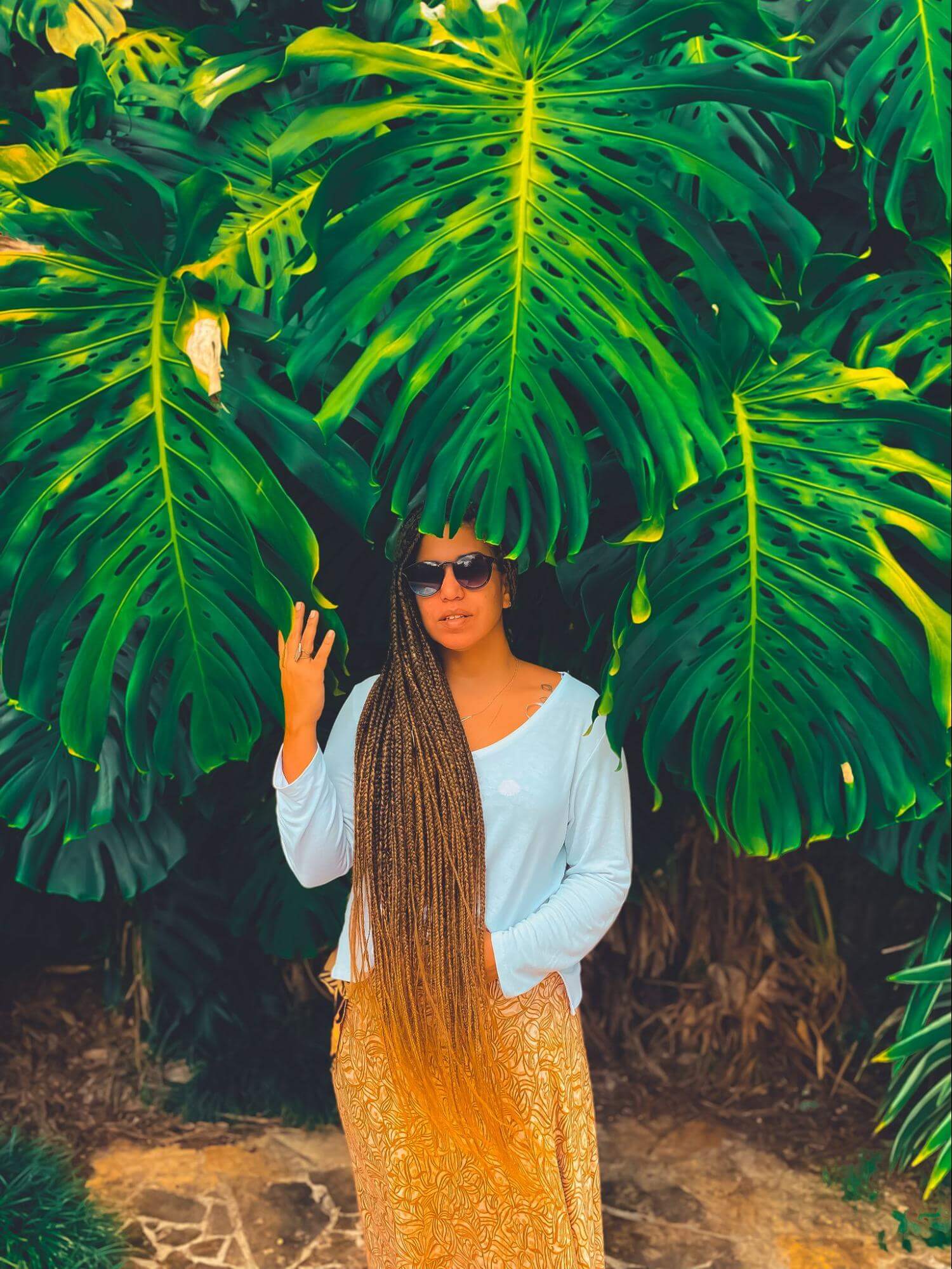 Duas imagens lado a lado, de uma mulher em pé entre grandes folhas. Na primeira com cores naturais e vivas, na segunda com cores bem verdes e laranja.