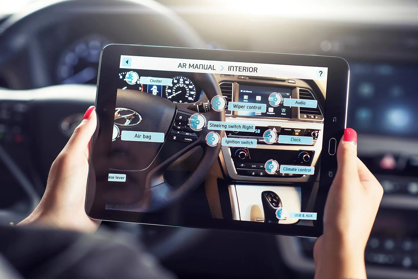 Imagem de uma pessoa segurando um tablet dentro do carro. Na tela do tablet, há a realidade aumentada mostrando os itens do painel do carro, como volante, botões e demais acessórios.