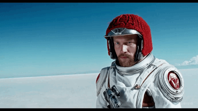 o gif representa um astronauta usando um capacete de lã vermelho em um deserto de sal