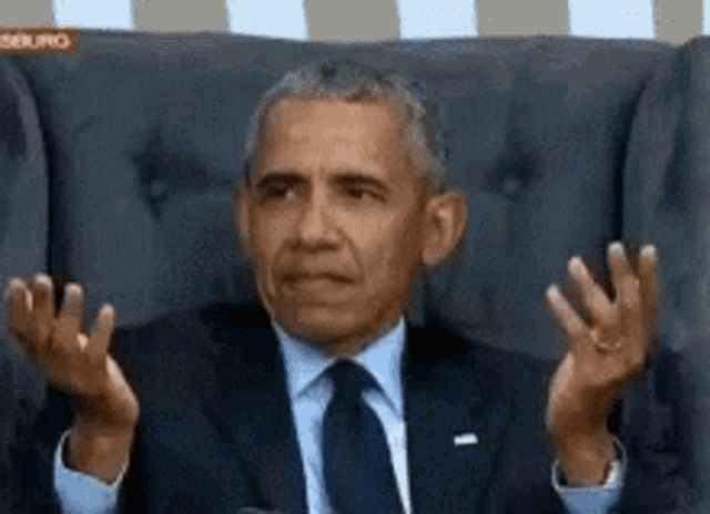 GIF: Barack Obama, ex-presidente dos EUA, está sentado em uma poltrona, levantando os braços com as mãos abertas. Ele olha para os dois lados com uma expressão de dúvida, como se estivesse perplexo ou não entendendo o que aconteceu. A imagem captura um momento de surpresa e reflexão.