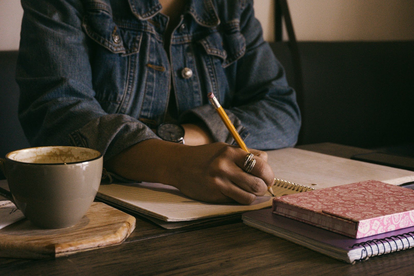 imagem de uma mulher escrevendo num caderno em cima da mesa