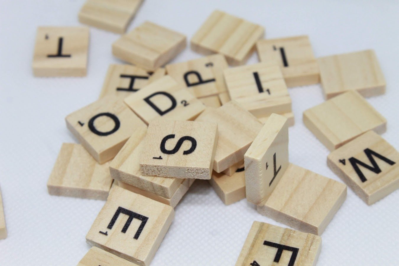 Várias peças de madeira estampadas com letras diversas espalhadas sobre uma superfície, partes de um jogo para formar palavras.