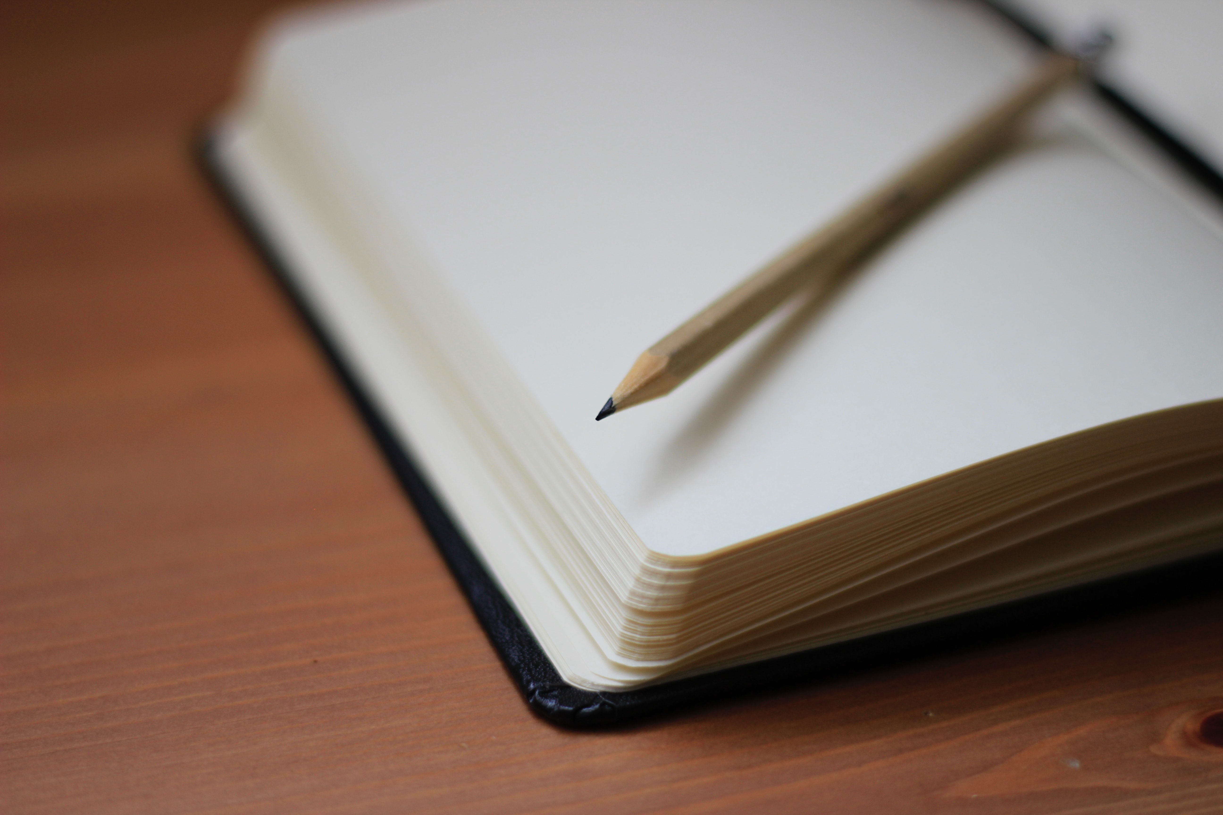 Imagem de um caderno aberto sobre uma mesa e com um lápis sobre a página aberta.