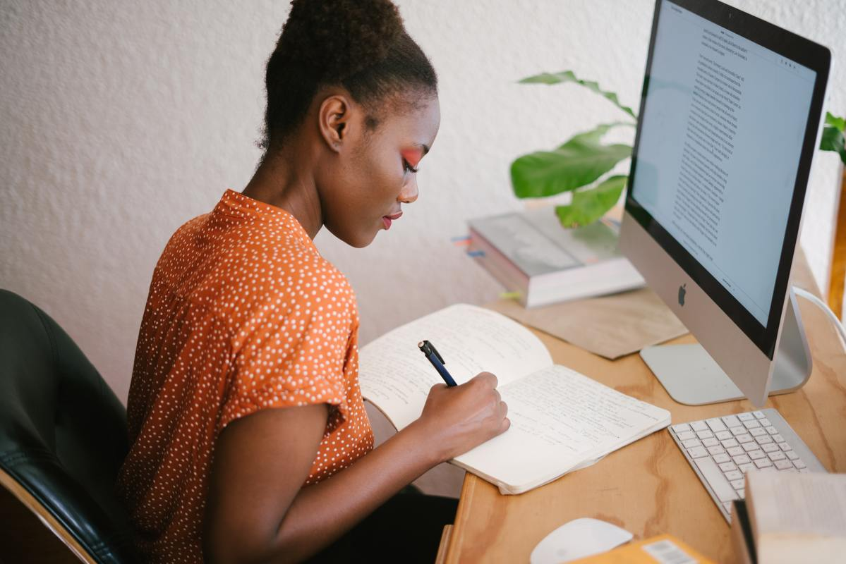 imagem de uma mulher fazendo anotações em frente a um computador