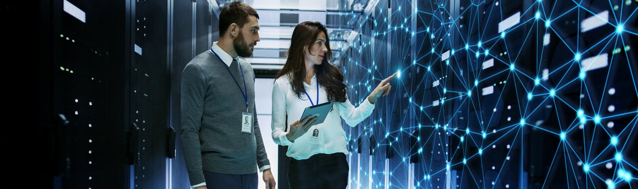 Duas pessoas engenheiras de TI discutindo detalhes técnicos em uma sala de servidores de trabalho com visualização de conexão à Internet.