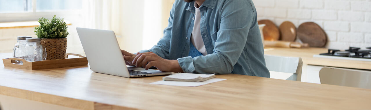 Imagem de uma pessoa de genêro masculino assistindo algo em um notebook que está posicionado sob uma mesa corporativa.