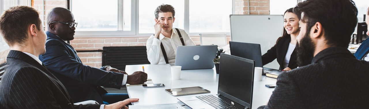 Pessoas sentadas em uma mesa corporativa discutindo ideias e fazendo análises.