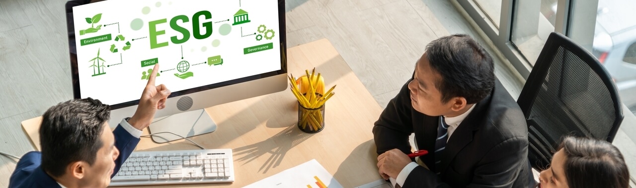 Dois homens e uma mulher sentados em uma mesa corporativa olhando para um computador escrito ESG na tela.