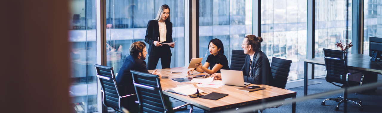 De cima, um grupo de colegas diversos em roupas formais discutindo ideias de negócios enquanto se reúnem à mesa no escritório moderno e trabalham juntos