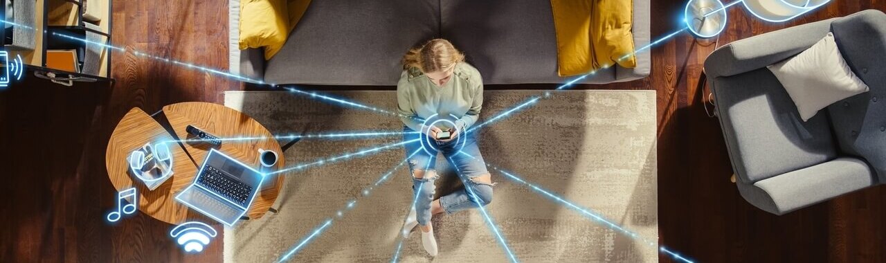 mulher sentada em um tapete mexendo no celular, com linhas que conectam o aparelho a outros elementos, representando conectividade e interenet das coisas - iot
