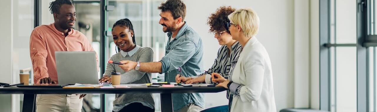 5 pessoas sentadas em torno de uma mesa alta, em frente a um computador, representando o treinamento de pessoas