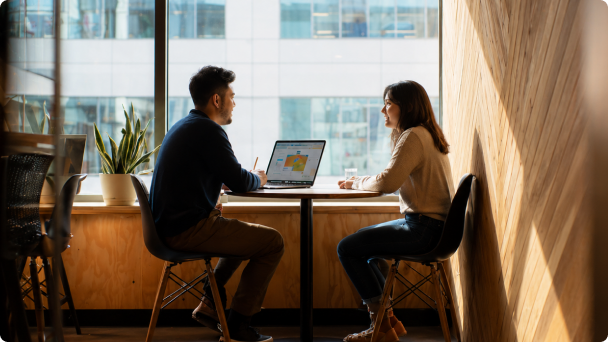 Duas pessoas conversando em uma mesa com notebook aberto