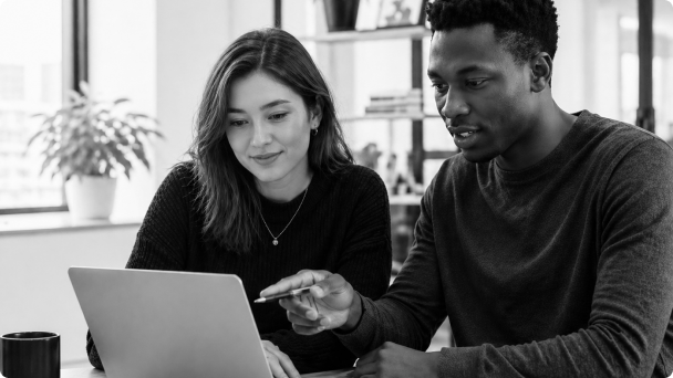 Duas pessoas analisando um notebook juntas em uma mesa